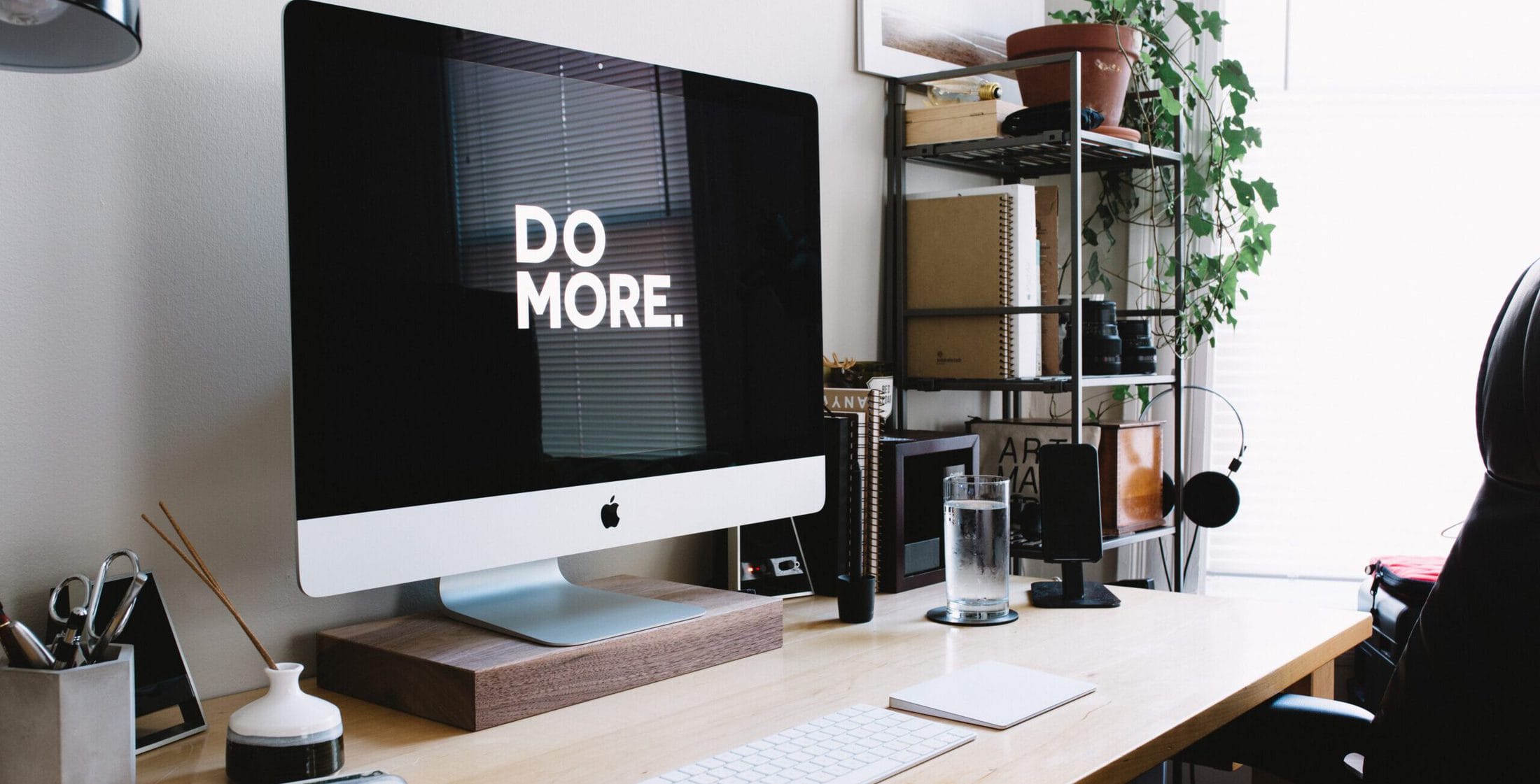 Ein iMac steht auf einem voll eingerichteten Schreibtisch. Davor stehen Tastatur und Maus. Auf dem Bildschirm steht " Do more" . Aus dem Artikel: Bewerbung