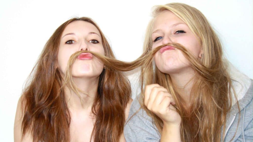 Zwei junge Frauen die die haare der einen geminsam als Schnurrbart verwenden. Aus dem Artikel: Warum wir aufhören sollten, für andere zu denken
