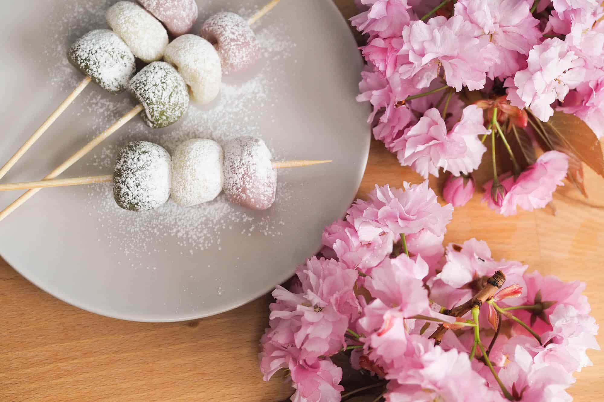 Hanami Dango japanische Klebreiskloesse neben Kirschblüten. Aus dem Artikel: Hanami Dango Rezept – Japanische Süßigkeit in Frühlingsfarben